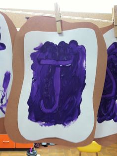 three pieces of paper with purple paint on them hanging from clothes pegs in front of a wall