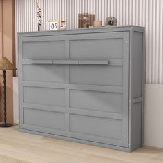 a grey dresser sitting on top of a hard wood floor next to a lamp and wall