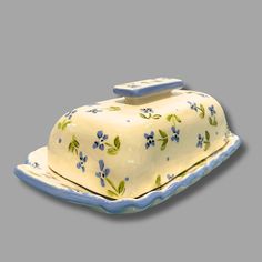 a white cake with blue flowers on it sitting on a platter in front of a gray background