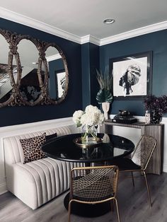 a dining room with blue walls and white chairs, black table and mirror on the wall