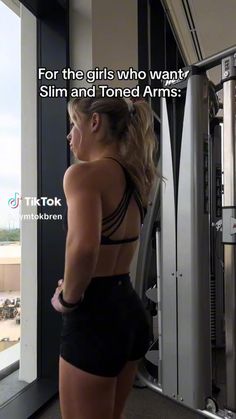 a woman standing in front of a gym machine looking out the window at an airport