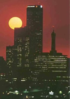 the sun is setting in front of some tall buildings with lights on at night time