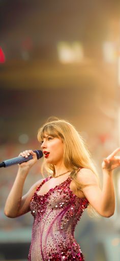 taylor swift performing on stage with microphone in her hand and red dress at the front