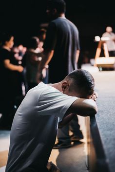 a man sitting on the ground with his head in his hands and people standing behind him