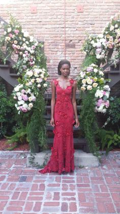 a woman in a red dress standing next to some white and pink flowers on a brick walkway