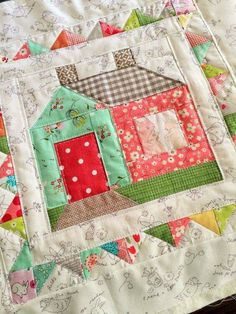 a close up of a quilt with a house on the front and green, red, yellow, orange, and pink colors