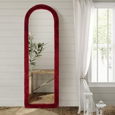 a large red mirror sitting on top of a wooden floor next to a white wall