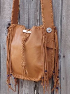 a brown leather bag hanging on a wooden fence with fringes and buttons attached to it