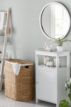 a white bathroom with a mirror, sink and storage basket next to the bathtub