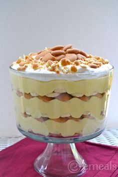 a layered cake with frosting and nuts in a glass dish on a pink place mat