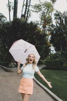 a woman is holding an umbrella in the air while walking down a brick path with palm trees behind her