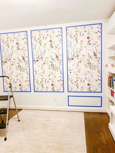 a living room with three paintings on the wall and a ladder in front of it