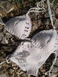 two white crocheted bikinisuits laying on the ground next to some rocks