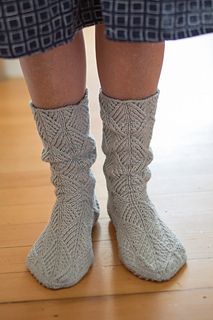 the legs and ankles of a person wearing gray knitted socks, standing on a wooden floor