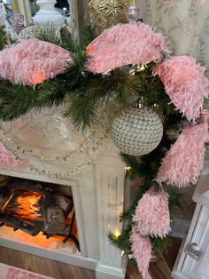 a fireplace decorated for christmas with pink feathers and ornaments on it's mantel