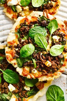 two flatbread pizzas topped with spinach leaves and ground meat on a cooling rack