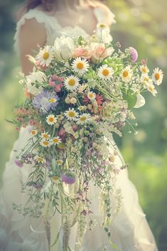 a woman in a wedding dress holding a bouquet of daisies and wildflowers