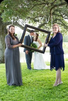 a bride and groom holding up a framed photo in front of their wedding party at the park