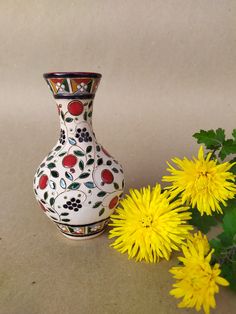 a white vase sitting next to yellow flowers on top of a brown surface with green leaves