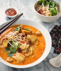 a bowl of food with chopsticks on the side and another bowl of soup in the background