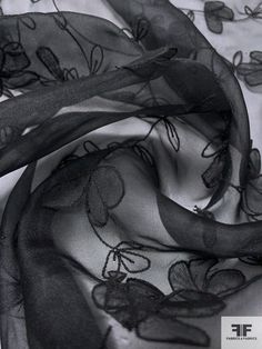 a black and white photo of a scarf with flowers on the bottom, in front of a bed sheet