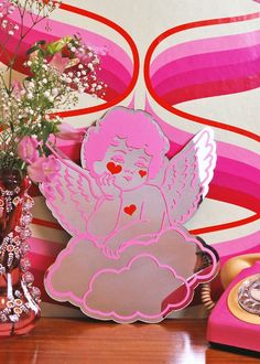 a pink angel sitting on top of a table next to a vase with flowers in it