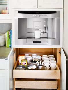 an open drawer with coffee cups and mugs in it on the side of a kitchen counter