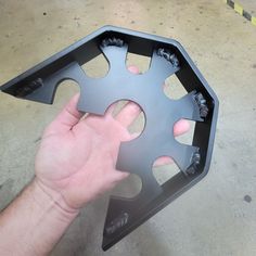 a hand is holding the bottom part of a metal object with holes and screws