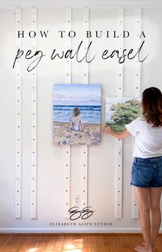 a woman standing in front of a white wall with a painting on it and the words how to build a peg wall easel