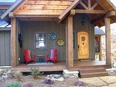 two red chairs sitting on the front porch of a small house with a yellow door