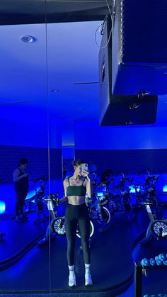 a woman standing in front of a mirror on top of a blue floor next to bikes