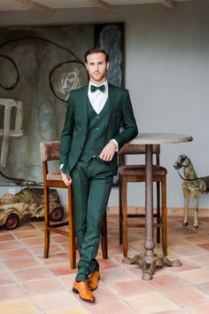 a man wearing a green suit and bow tie standing in front of a wooden table