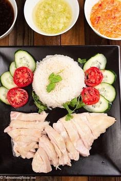 a black plate topped with meat and veggies next to bowls of sauces