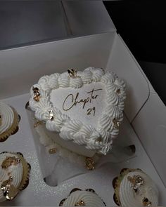 a white heart shaped cake in a box surrounded by cupcakes