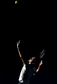 a tennis player is reaching up to hit the ball with his racket on a dark court