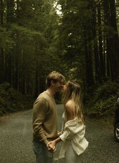 a man and woman are standing in the middle of a road with trees behind them