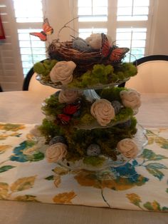 a three tiered cake with flowers and butterflies on it's top, sitting on a table