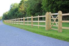 a wooden fence along the side of a road with grass and trees in the background