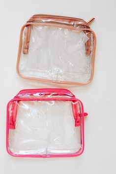 two clear bags sitting next to each other on top of a white table with pink handles