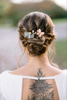 the back of a woman's head with tattoos on her chest and flowers in her hair