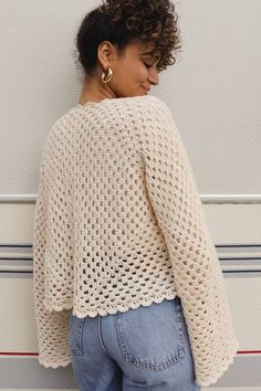 a woman standing against a wall with her back to the camera, wearing a crocheted sweater