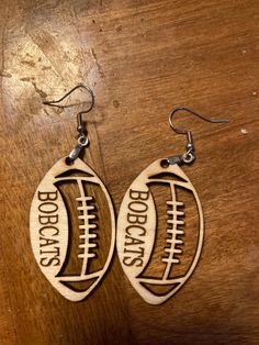 two wooden earrings with footballs engraved on the front and back, sitting on a table