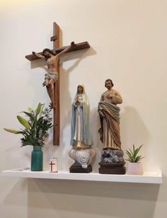 three statues of jesus and mary on a white shelf with plants in front of it