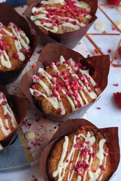 four cupcakes with white frosting and sprinkles on them sitting on a table