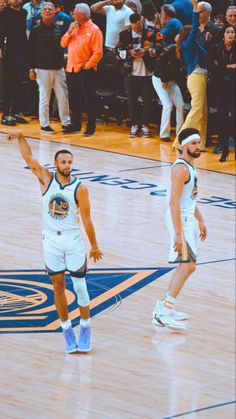 two basketball players standing on a court with their arms in the air and people watching