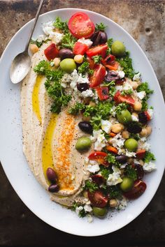 a white plate topped with food next to a bowl of olives and tomatoes