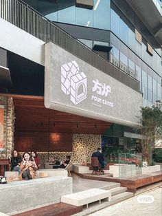 people are sitting on concrete benches in front of a building with a sign that reads four cubes