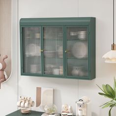 a green cabinet sitting on top of a desk next to a potted plant and lamp