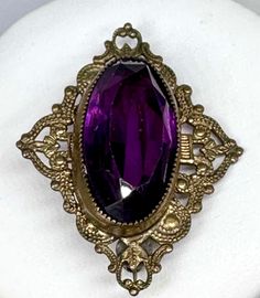 This lovely glass and brass gold plated or gilt antique brooch is in fabulous condition with very little wear for its age. This brooch features a large oval faceted glass stone in a rich purple amethyst color. Estimated late 1800s. Art nouveau, Victorian period. Antique Purple Formal Brooches, Antique Purple Brooches For Formal Occasions, Purple Victorian Wedding Brooches, Antique Purple Brooches As Gift, Vintage Purple Oval Brooch, Vintage Purple Wedding Brooches, 1800s Art, Victorian Period, Rich Purple