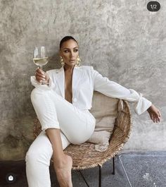 a woman sitting on a wicker chair holding a glass of white wine in her hand